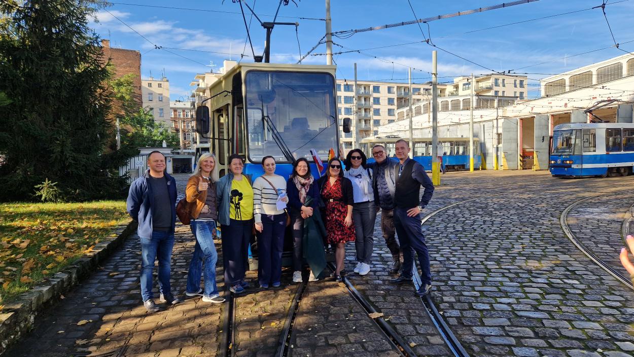 A group of people posing for a picture in form of a tram with tram depot building in the background