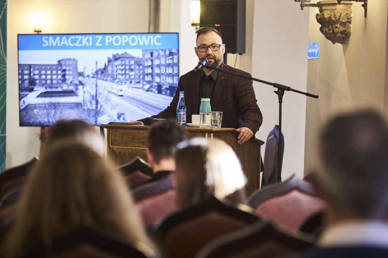 People listening to the lecture about Popowice Depot, historical photo on the screen behind.