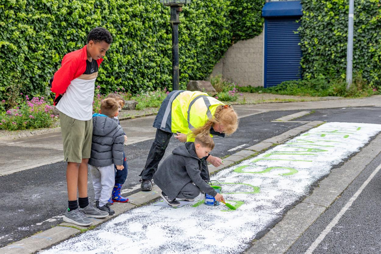 Children and a woman in high-visibility jacket painting the street where the wall used to stand.