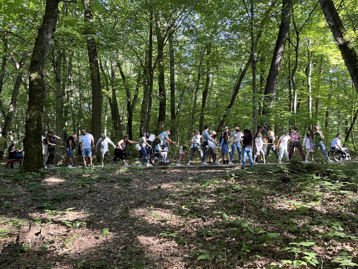  The image shows the 32 participants holding on to each other while doing one of the retreat exercises in a forest context.