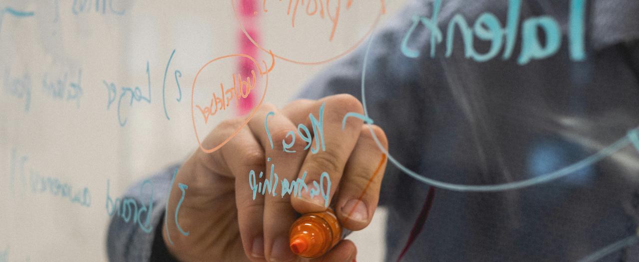 Person writing with a permanent marker on a transparent blackboard