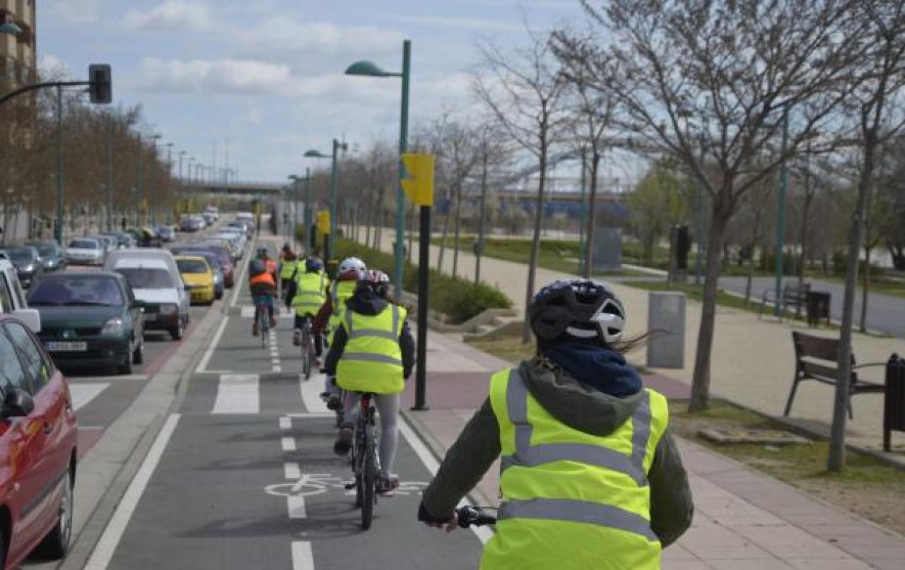 Oameni în jachete de înaltă vizibilitate, mergând cu biciclete pe o bandă dedicată pentru biciclete lângă mașini într-un ambuteiaj. Zaragoza, Spania