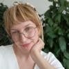 Blond female person in white blouse wearing glasses, plant background