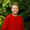 Kalle smiling in red sweater and green, leafy background
