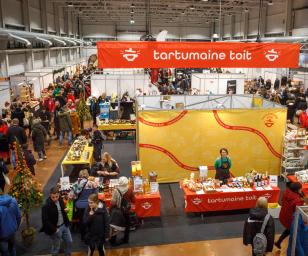 This image depicts a bustling indoor market or fair, likely focused on food and local products.