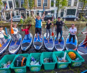  A group of people participating in a canal cleanup activity using paddleboards. 