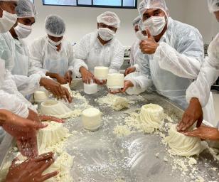 A group of people in a professional or educational setting, engaged in the hands-on preparation of a dairy product