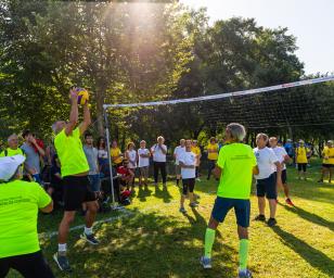 Vibrant scene of a community volleyball game, with players actively engaged in the sport and spectators enjoying the event in a pleasant outdoor environment.