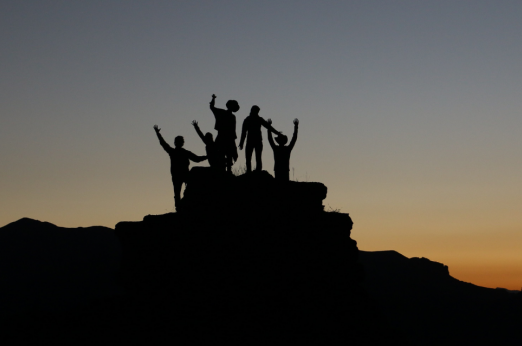 Group of people on top of a mountain with a sunset in the background.