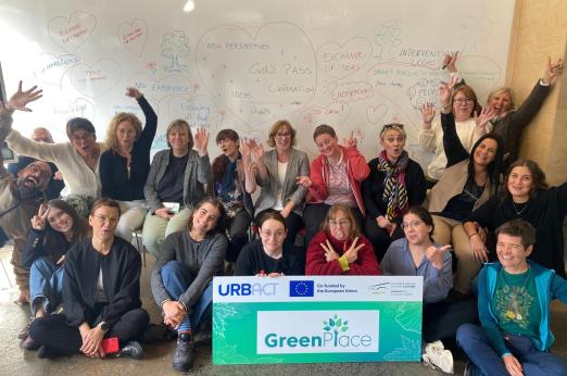 A happy group picture of the GreenPlace partner in front of the whiteboard with thoughts about the project and the URBACT and GreenPlace logos on a banner in front of the group. 