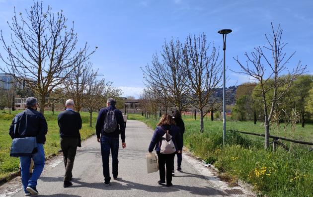 A group of five people walking on a paved pathway in a green urban area. 