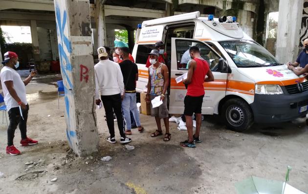 A moment of community healthcare provision in an urban setting, with an ambulance and medical personnel attending to the needs of the local residents.