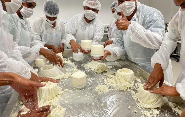 A group of people in a professional or educational setting, engaged in the hands-on preparation of a dairy product