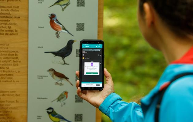 A person in an outdoor setting using a smartphone to scan a QR code on a wildlife informational signboard