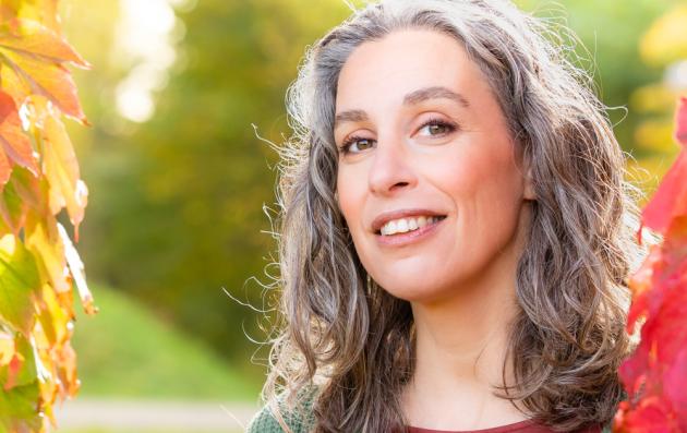 Female with curly grey hair before a red and green autumn background