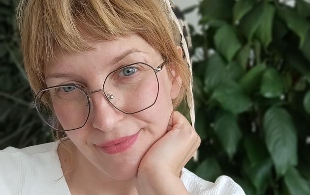 Blond female person in white blouse wearing glasses, plant background