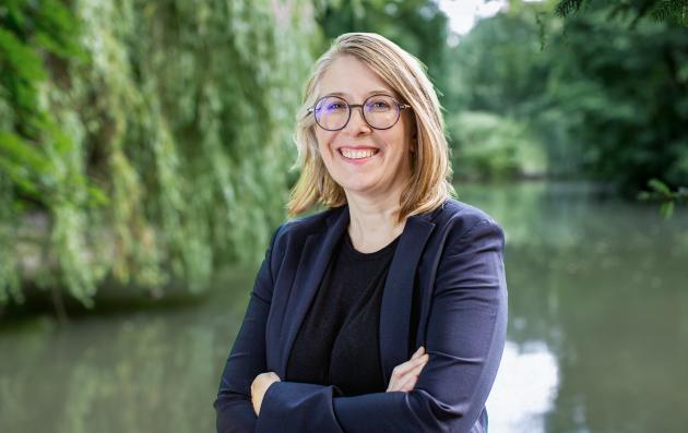 Franziska Singer, a blonde woman with glasses wearing a suit, standing by a lake