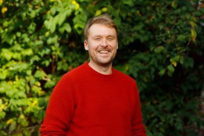 Kalle smiling in red sweater and green, leafy background