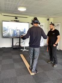 A person wearing Vr glasses, standing on a wood board in front of a screen