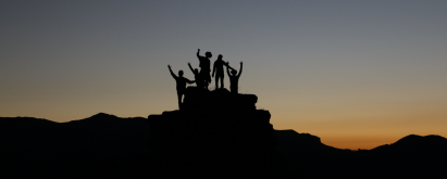 Group of people on top of a mountain with a sunset in the background.