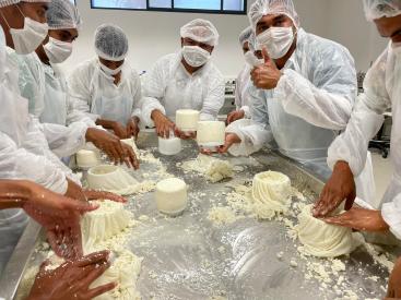 A group of people in a professional or educational setting, engaged in the hands-on preparation of a dairy product