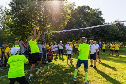 Vibrant scene of a community volleyball game, with players actively engaged in the sport and spectators enjoying the event in a pleasant outdoor environment.