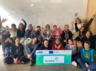 A happy group picture of the GreenPlace partner in front of the whiteboard with thoughts about the project and the URBACT and GreenPlace logos on a banner in front of the group. 