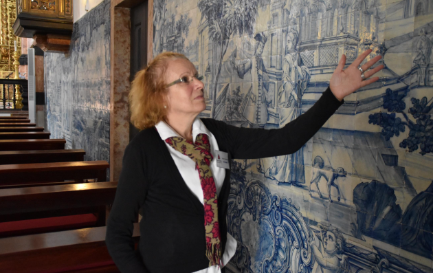 A woman indicating a painting on a wall of a building.